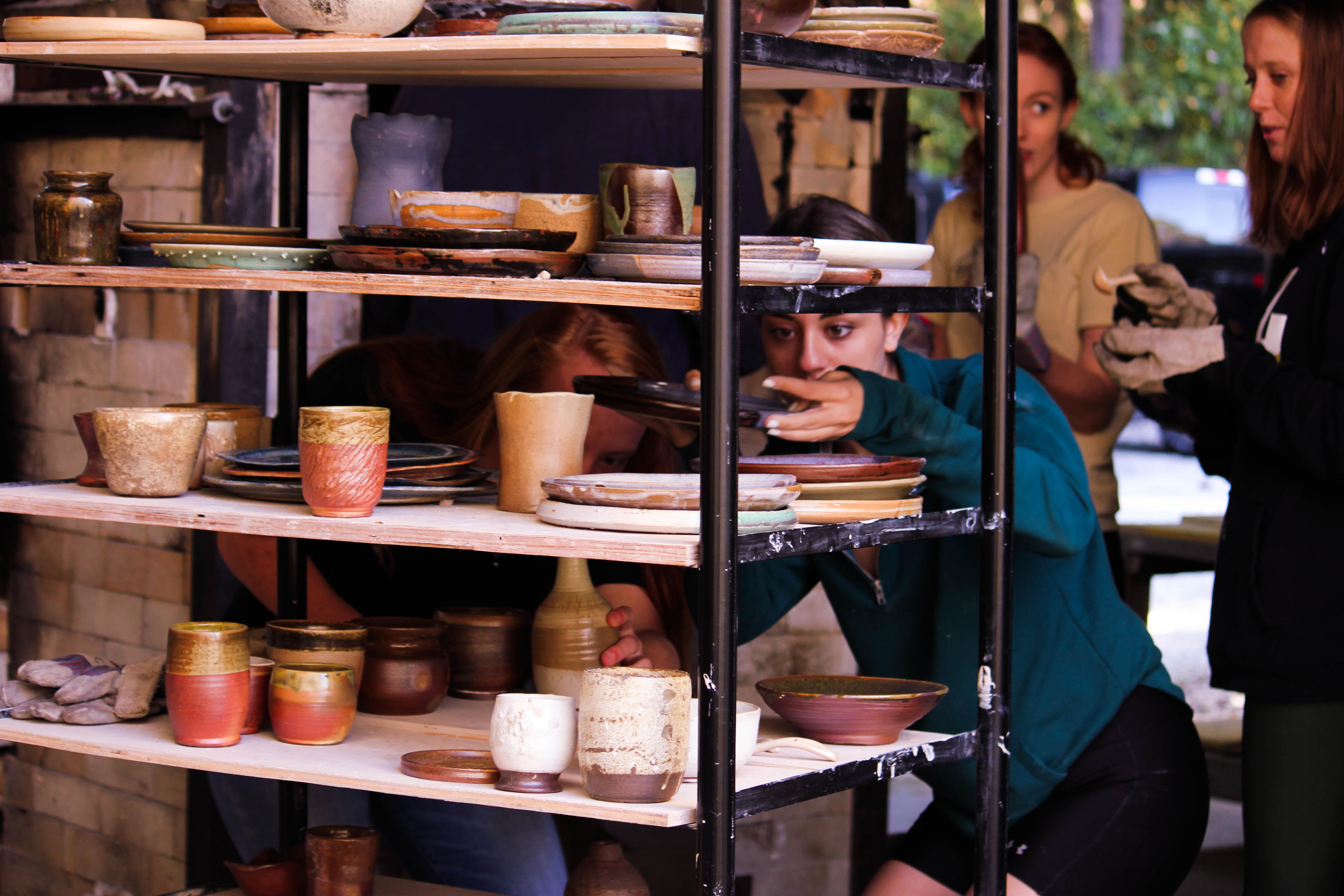 陶艺学生从木窑里卸下来，把作品放在运输工具的架子上.