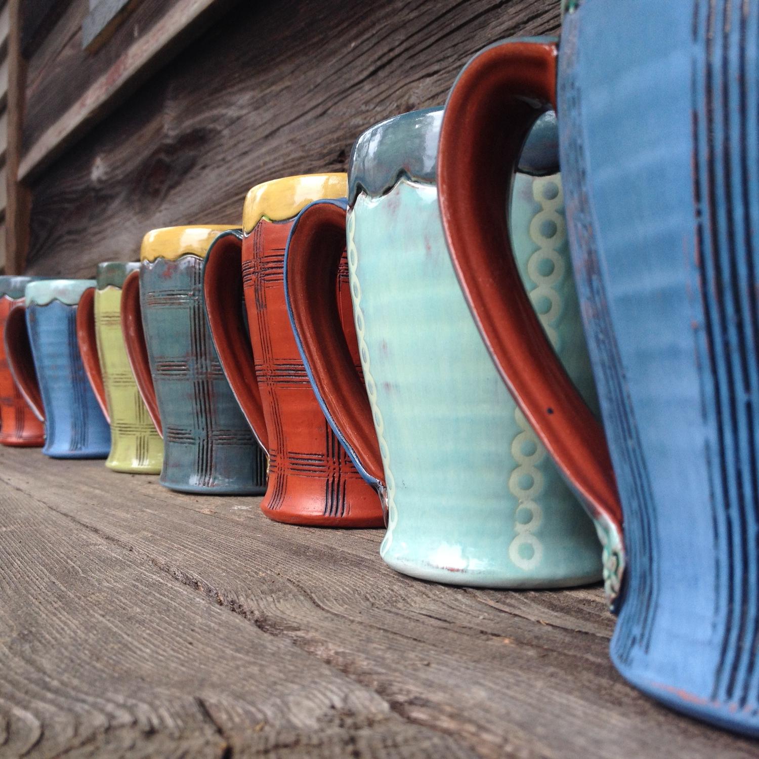 艺术家艾米·桑德斯创作的一排充满活力的彩色陶瓷咖啡杯.